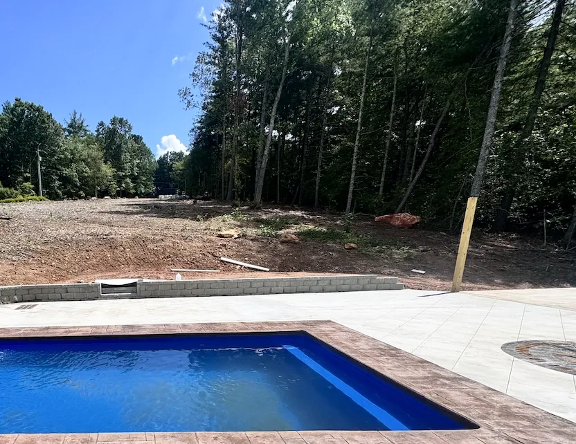 Block retaining wall holding back a graded slope next to a pool and concrete deck on a wooded property